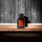 Schwarzer Flakon Acqua di Parisis Oud Couture Parfum auf Holztisch vor Holzwand