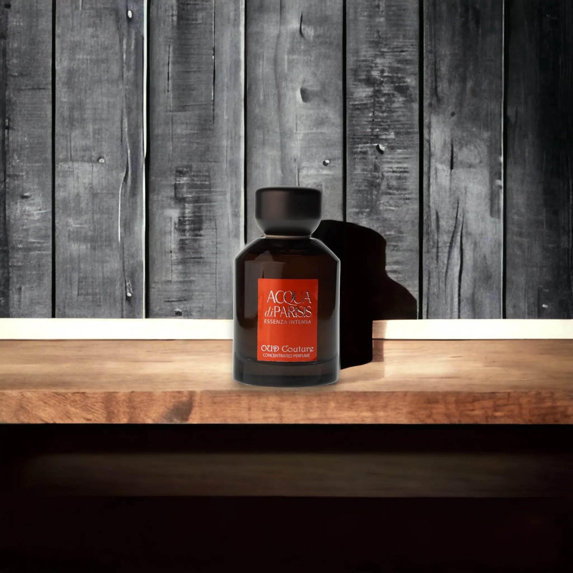 Schwarzer Flakon Acqua di Parisis Oud Couture Parfum auf Holztisch vor Holzwand