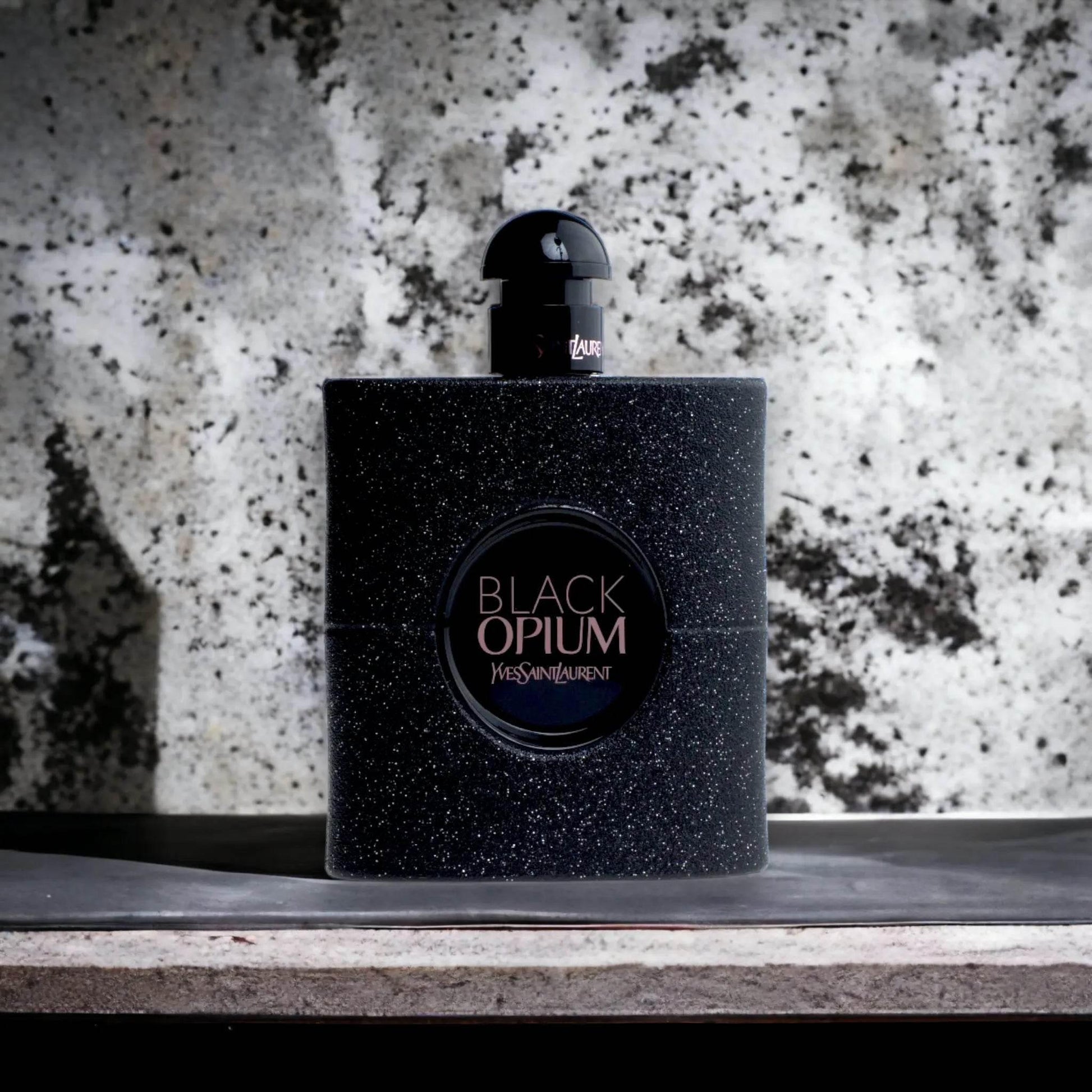 Schwarzer, glitzernder Parfumflakon Black Opium vor marmoriertem Hintergrund