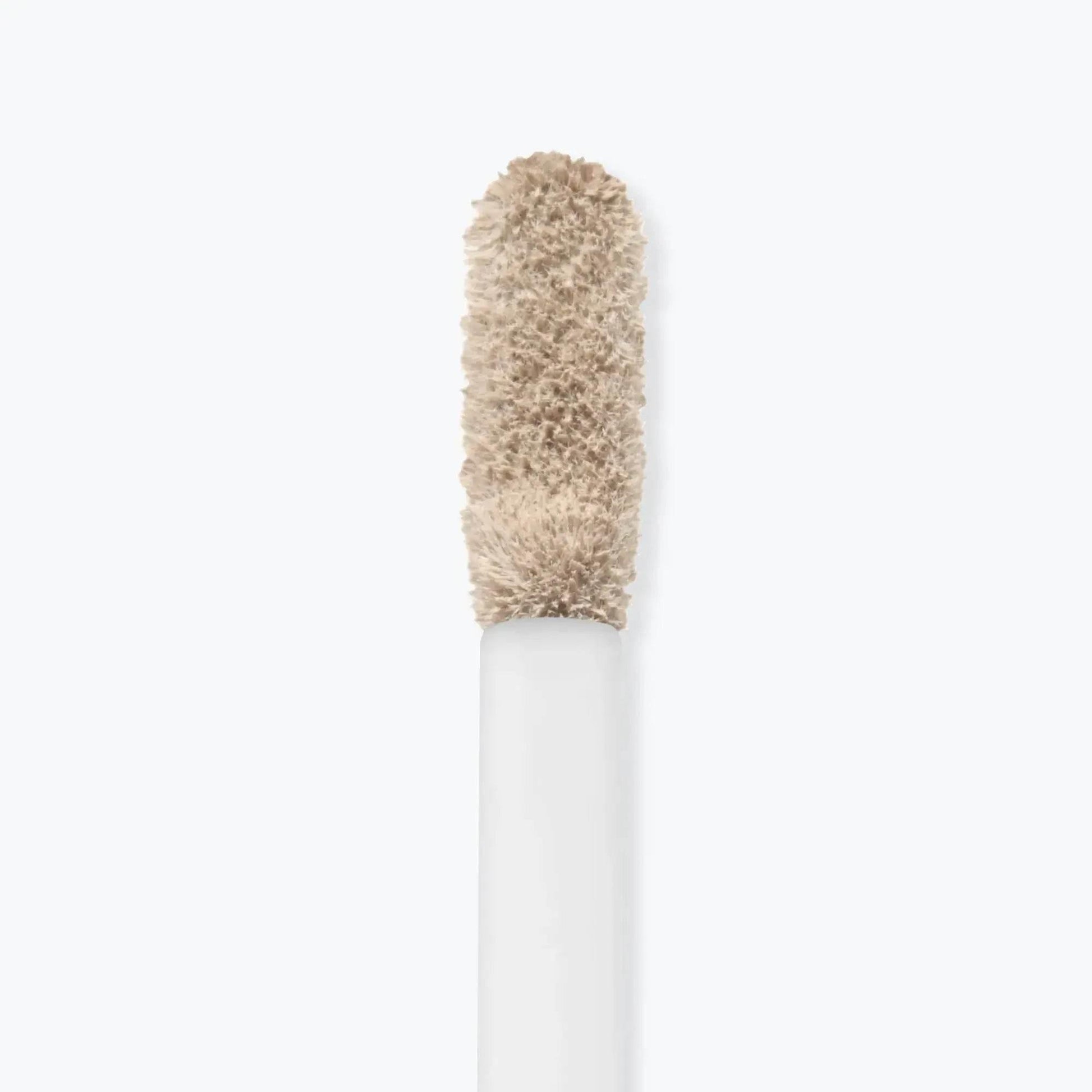 Nahaufnahme eines Concealer-Applikators mit beiger, cremiger Textur auf weißem Hintergrund.