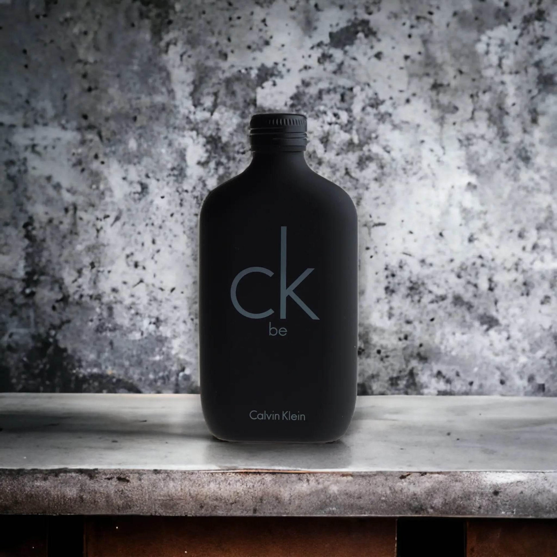 Schwarzer Flakon CK Be Eau de Toilette auf grauem Steinuntergrund, minimalistisches Design