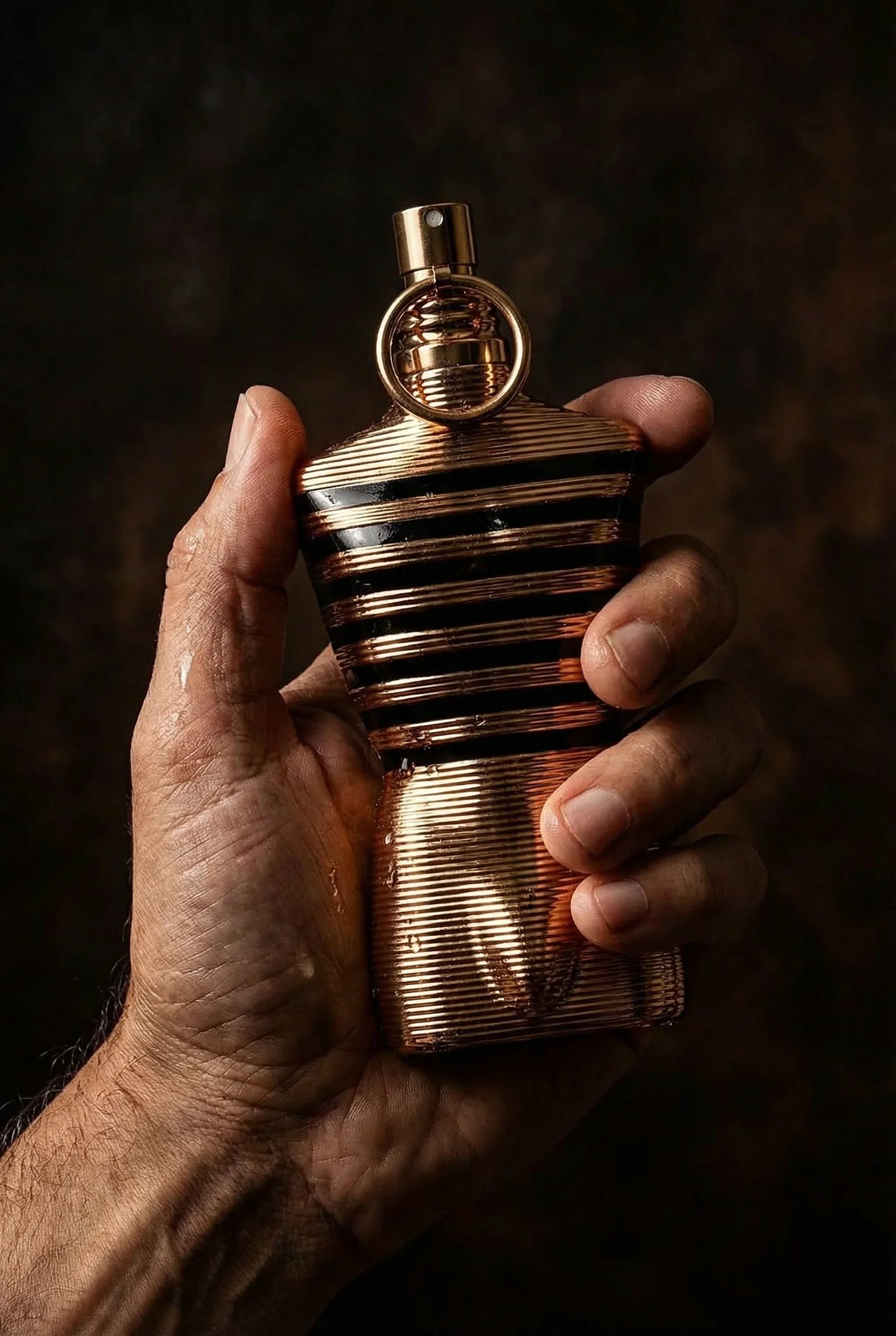 Nahaufnahme einer Hand hält eine goldene, maskuline Parfumflasche mit Streifen-Design