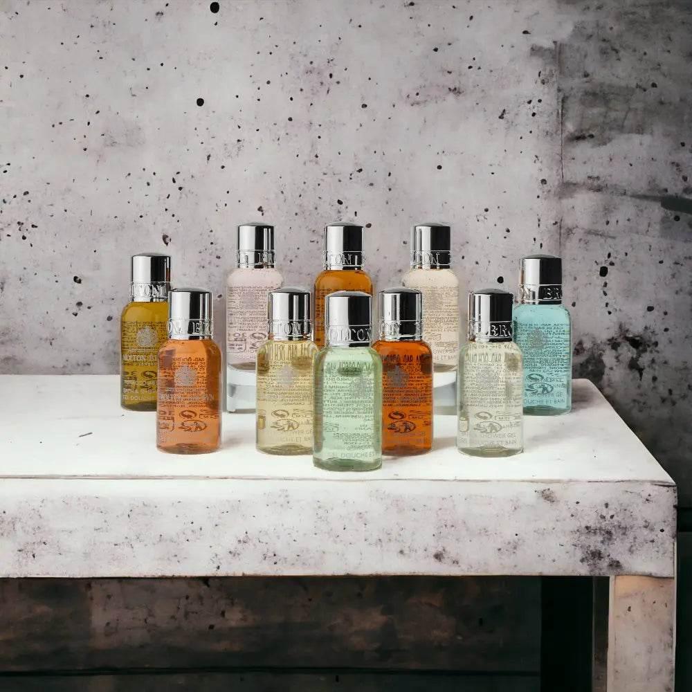 Neun verschiedene Flaschen Body Care Produkte stehen auf einem weißen Tisch vor Betonwand.