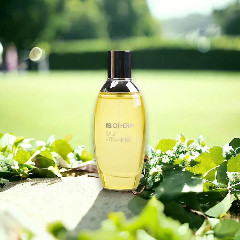 Gelbe Biotherm Eau Vitaminée Parfumflasche, draußen mit grünen Blättern, sonnig