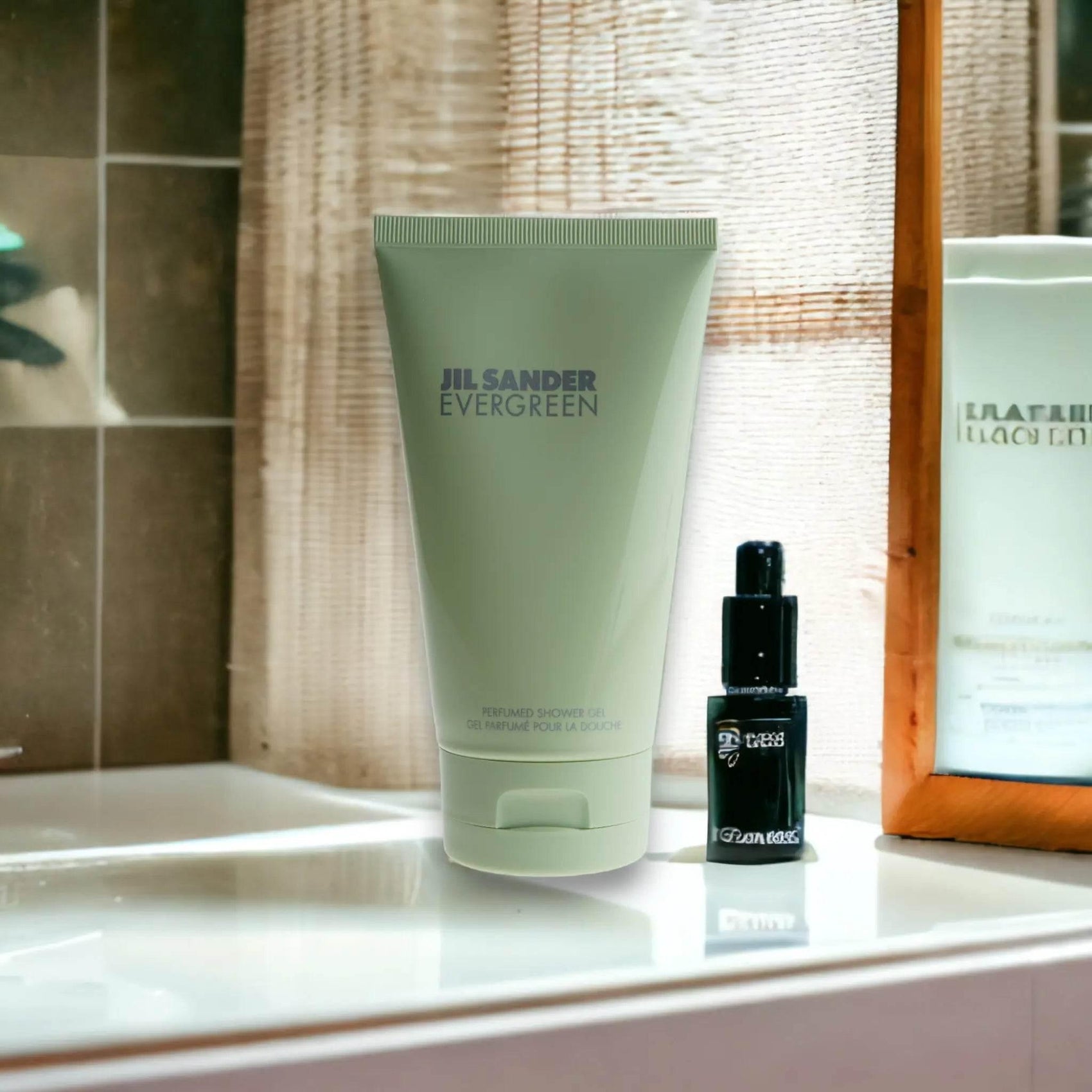 Jil Sander Evergreen Duschgel Tube auf Waschbecken im Badezimmer, daneben ein kleines schwarzes Fläschchen.