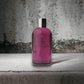 Pinkfarbenes Duschgel in transparenter Flasche mit silbernem Deckel auf Betonuntergrund