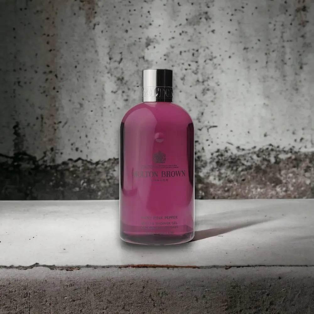 Pinkfarbenes Duschgel in transparenter Flasche mit silbernem Deckel auf Betonuntergrund
