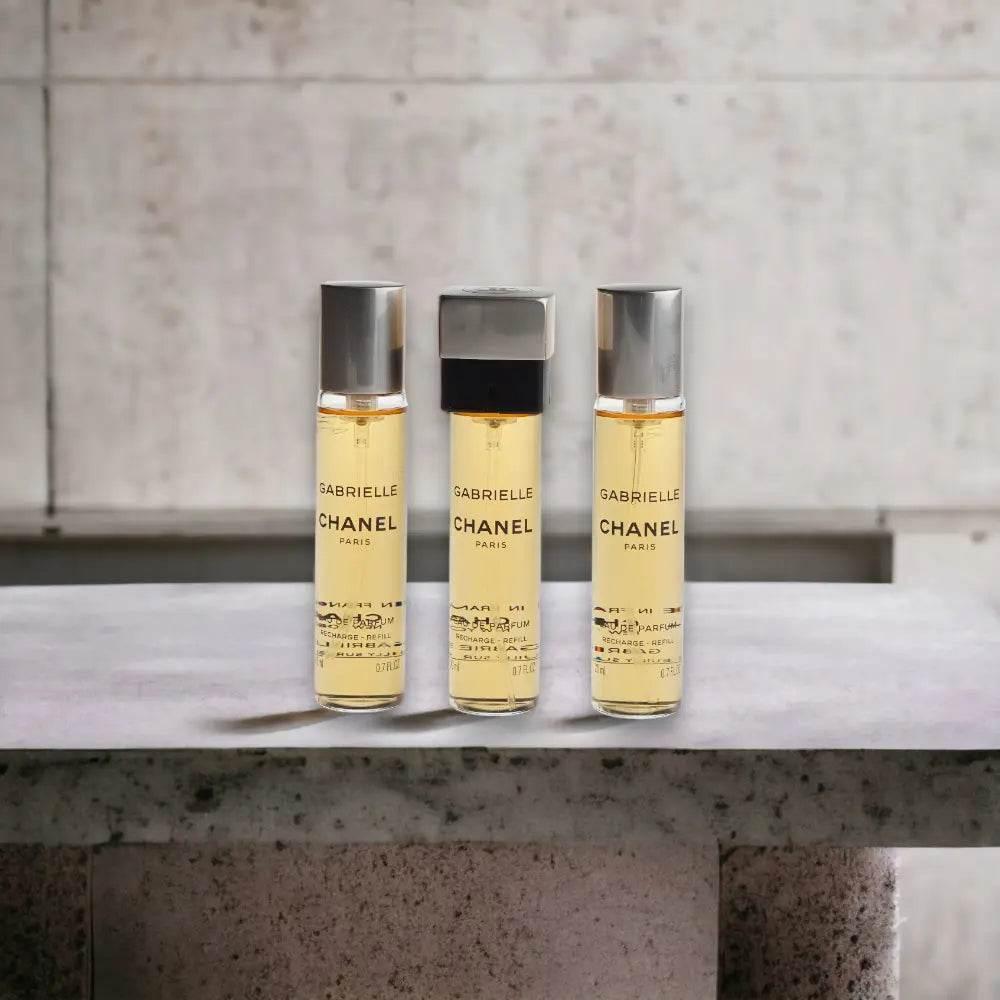 Drei Flakons Gabrielle Parfum Spray mit silbernen Kappen auf Betonoberfläche