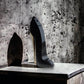 Schwarzer High Heel Parfümflakon mit goldener Sohle auf Marmor vor Betonwand
