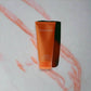 Orangefarbene Clinique Happy Duschgel Tube auf hellem Hintergrund mit rosa Linienmuster.