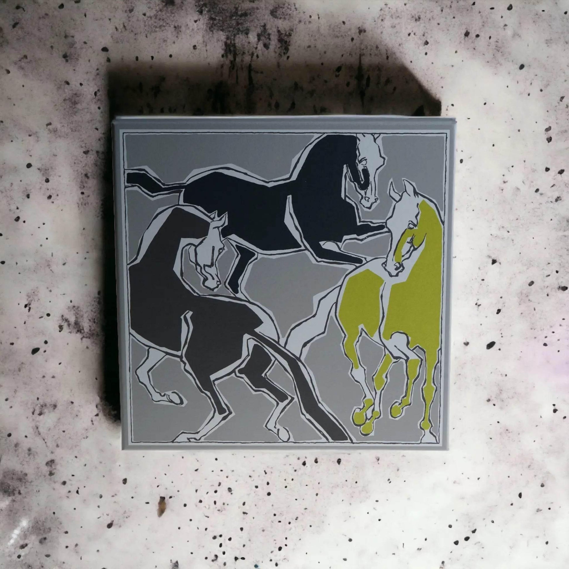 Parfümset-Verpackung mit stilisierten Pferden in Grau, Schwarz und Gelb auf marmoriertem Hintergrund.