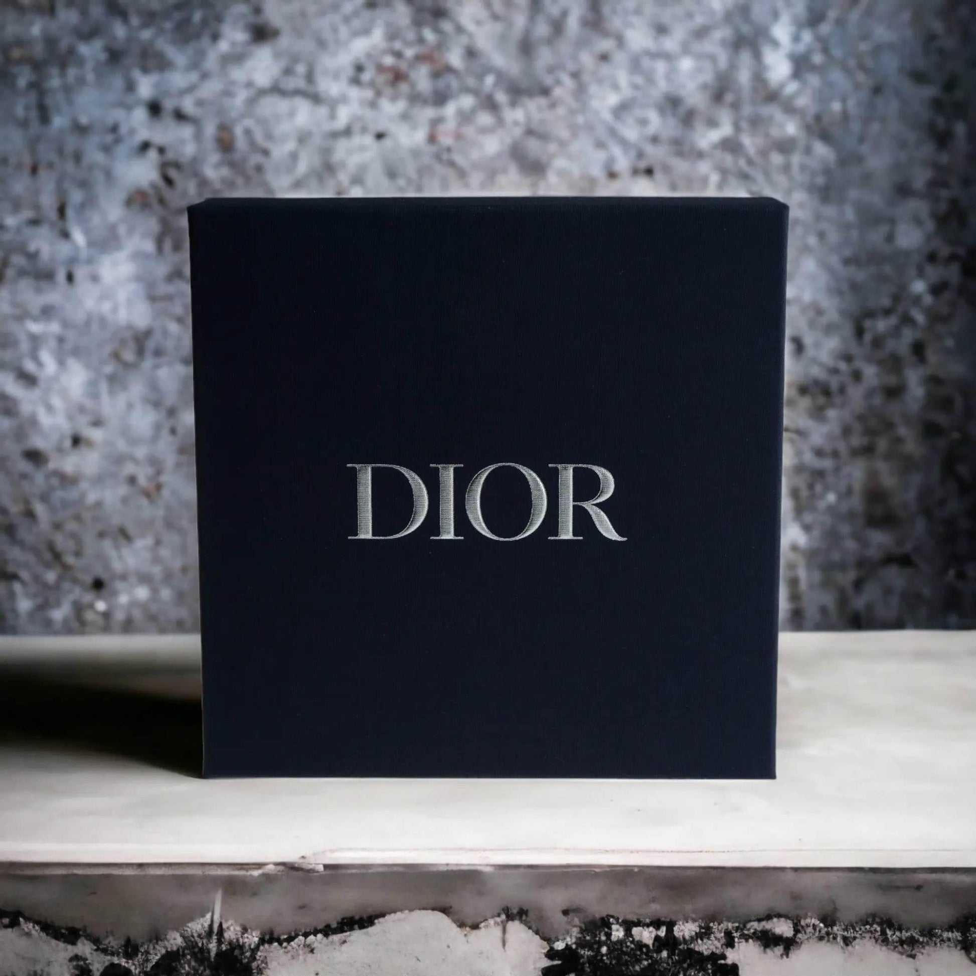 Schwarze Geschenkbox mit silbernem DIOR-Logo, luxuriöses Herren Duftset vor Steinwand