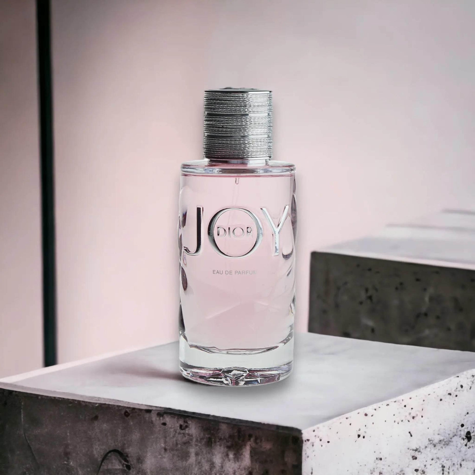 JOY Eau de Parfum Flakon mit rosafarbenem Duft auf hellem Podest, modernes Design