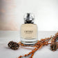 L’Interdit Eau de Parfum Flakon auf hellem Untergrund mit Tannenzapfen und Trockenblumen