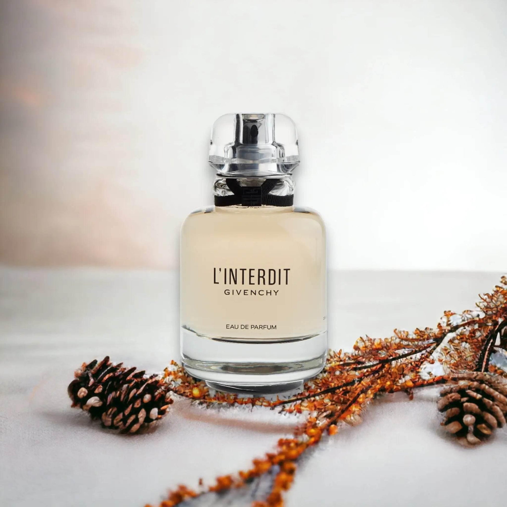 L’Interdit Eau de Parfum Flakon auf hellem Untergrund mit Tannenzapfen und Trockenblumen