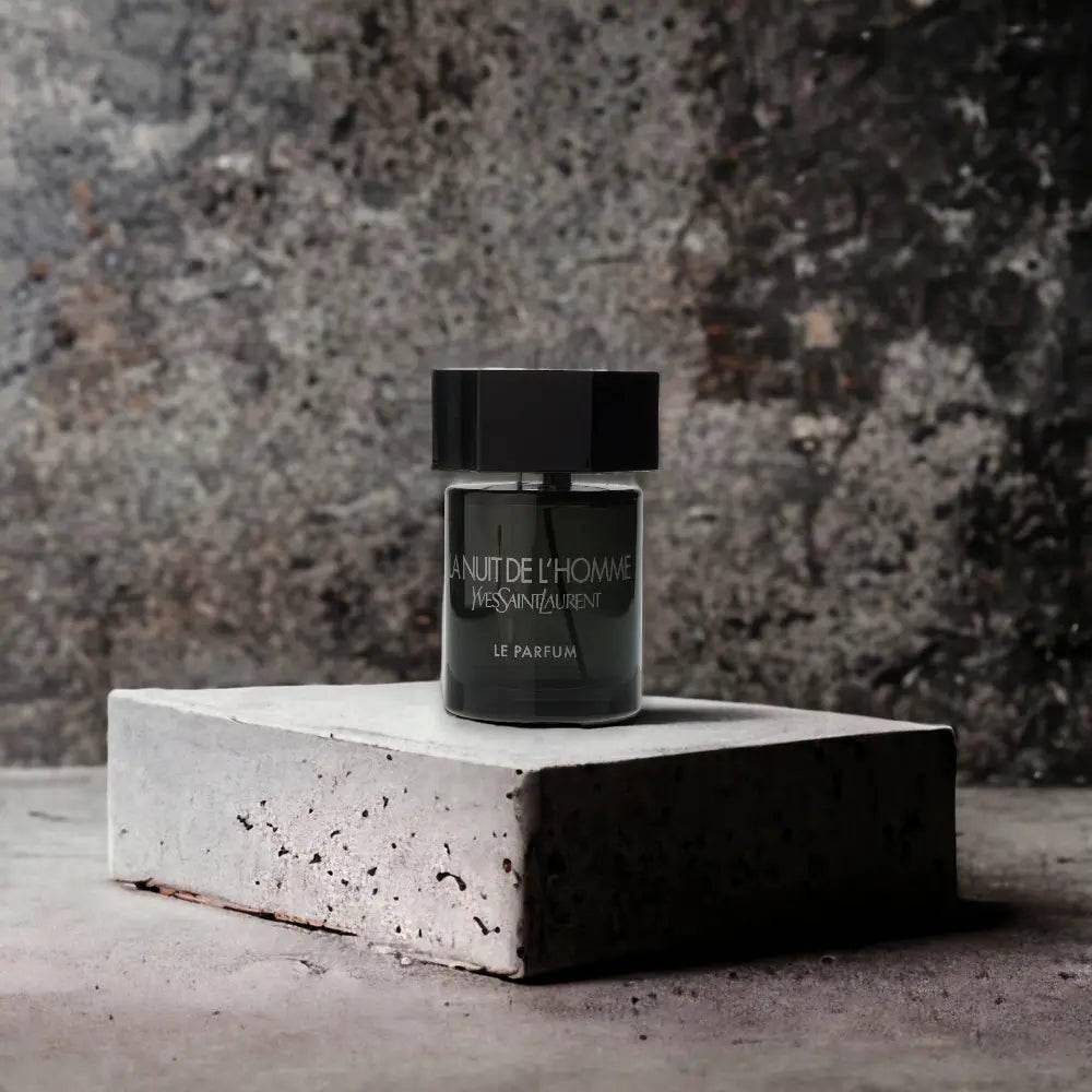 Schwarzer Flakon La Nuit de L'Homme Parfum auf Betonsockel vor dunklem Hintergrund