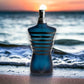 Dunkelblauer Parfumflakon in Torsoform mit Streifen, am Strand vor Sonnenuntergang