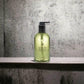 Molton Brown Handseife Lime & Patchouli in grüner Pumpflasche vor Betonwand