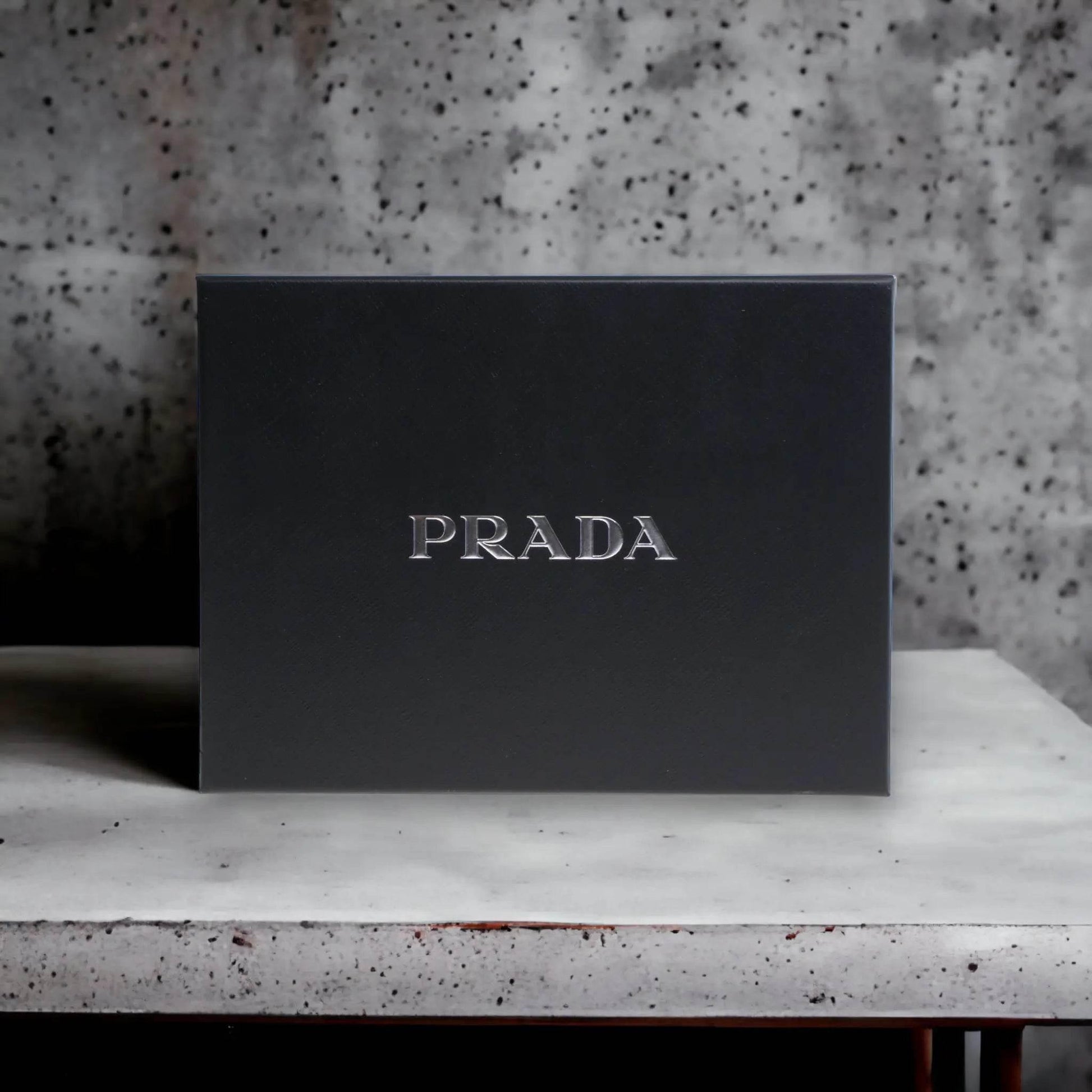 Elegante schwarze Parfum-Geschenkbox mit silbernem PRADA-Logo auf Steinoberfläche