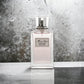 Miss Dior Körper-Spray in rechteckigem Glasflakon mit silbrigem Etikett vor grauem Hintergrund