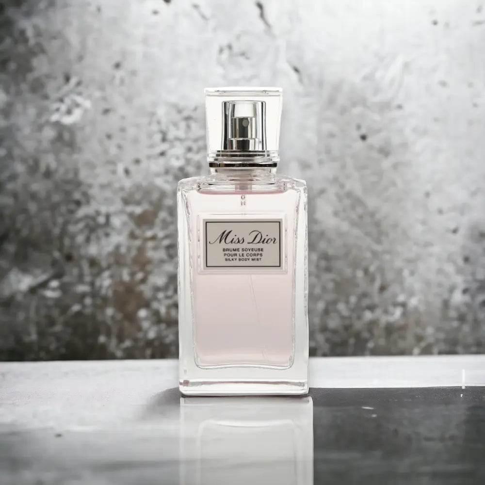 Miss Dior Körper-Spray in rechteckigem Glasflakon mit silbrigem Etikett vor grauem Hintergrund