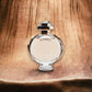 Runder Flakon Olympea Eau de Parfum auf strukturierter Holzoberfläche, Luxusduft