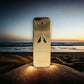 Goldenes Parfum One Million Elixir Flakon auf Sand vor Sonnenuntergang am Meer