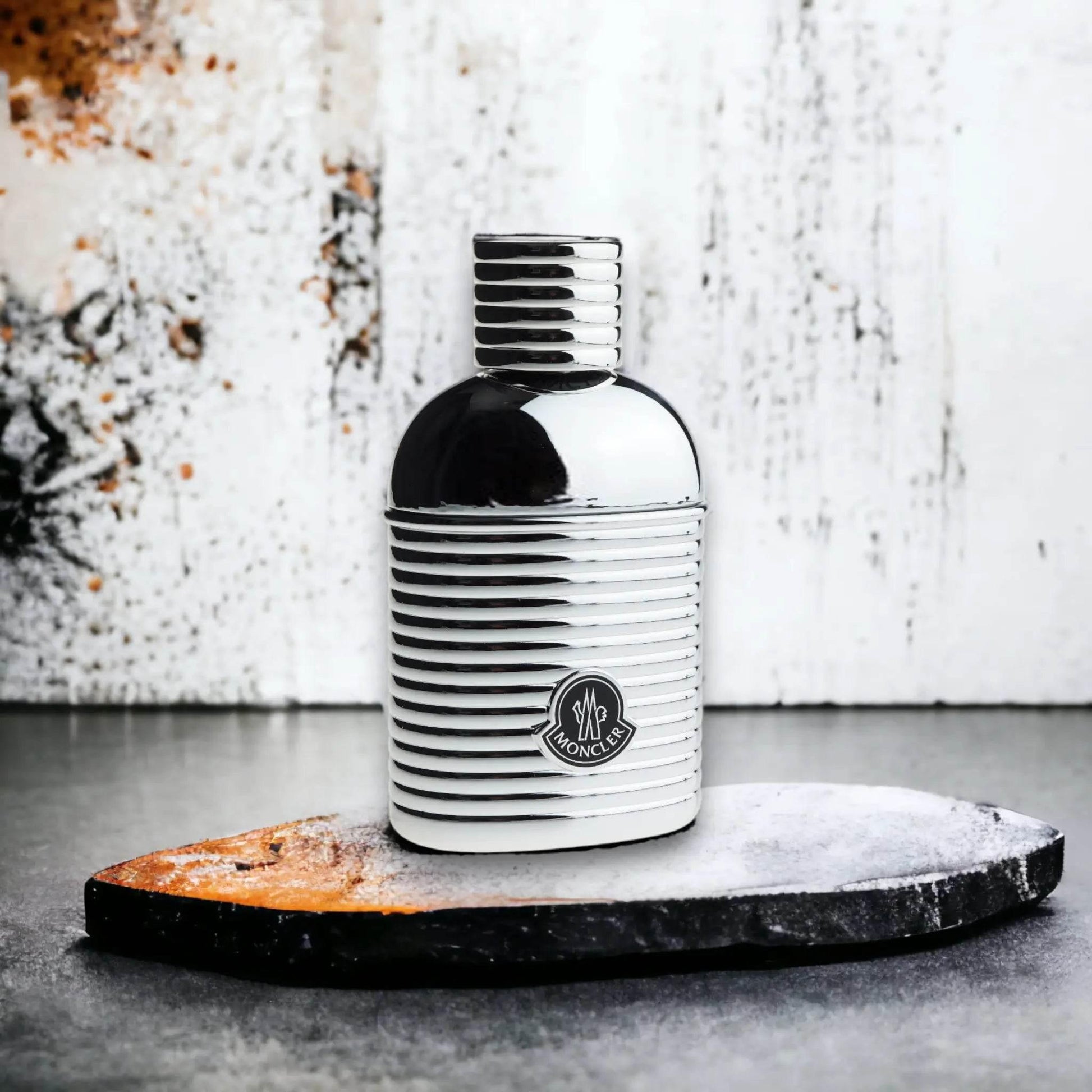 Silbernes Herren Parfumflakon mit Moncler-Logo auf Steinplatte, moderner Hintergrund.