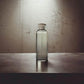 Klares Parfumflakon mit weißem Verschluss, minimalistisch auf Steinoberfläche inszeniert.