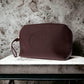 Bordeauxrote Kosmetiktasche aus Leder mit 'THE BRIDGE' Prägung, auf steinernem Tisch.