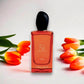 Rotes Parfumflakon Si Passione Éclat mit schwarzen Verschluss, umgeben von orange-gelben Tulpen, vor weißem Hintergrund.