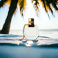 Parfümflakon mit goldener Kappe am Strand, Palme im Hintergrund, sonnige Atmosphäre