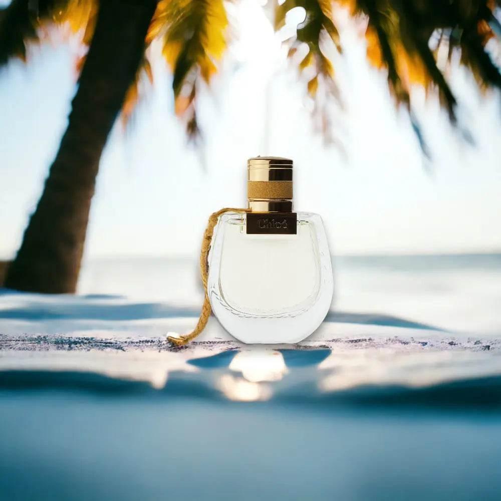 Parfümflakon mit goldener Kappe am Strand, Palme im Hintergrund, sonnige Atmosphäre