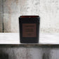 Schwarze Duftkerze Tuscan Leather von Tom Ford vor grauer Betonwand, Luxus Raumduft