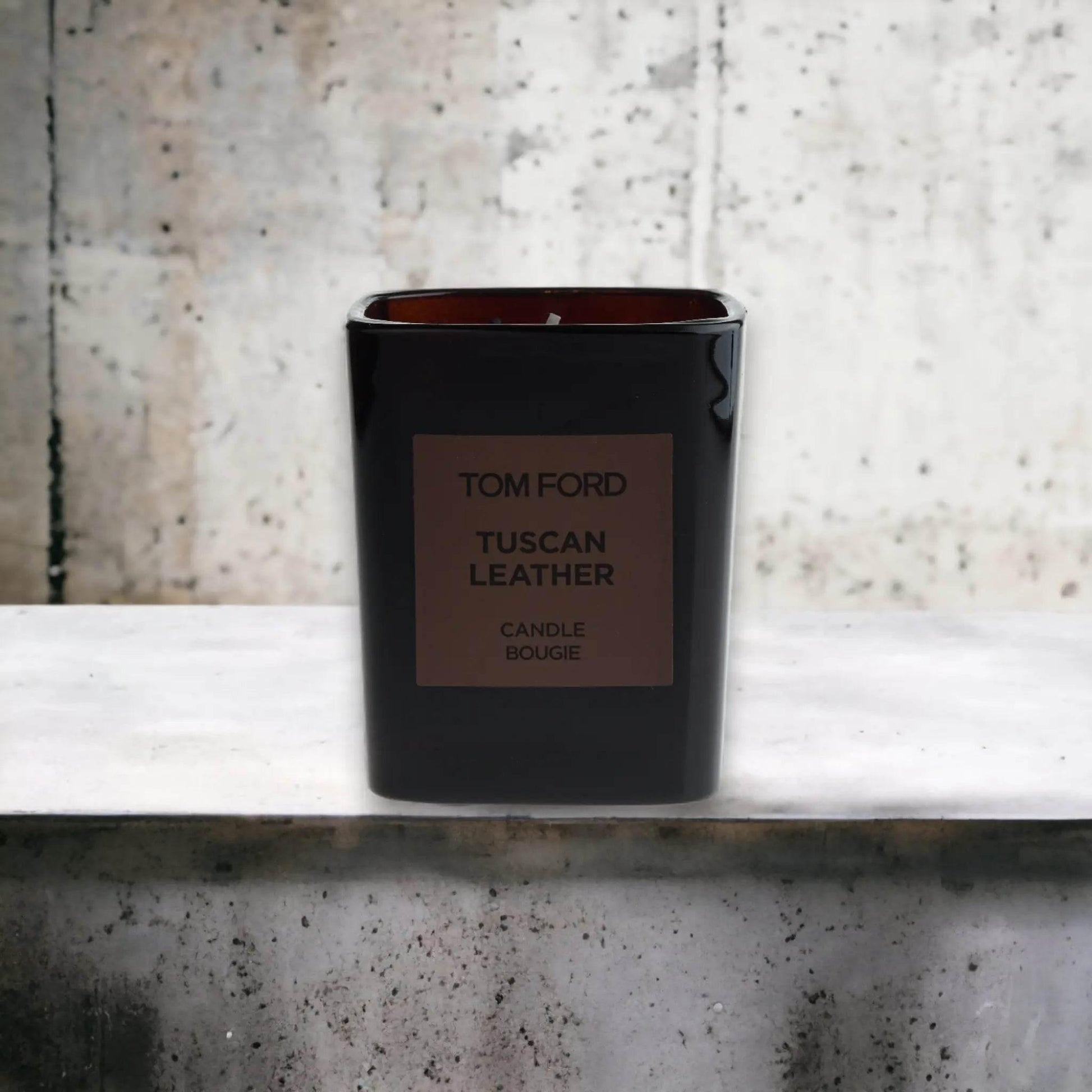 Schwarze Duftkerze Tuscan Leather von Tom Ford vor grauer Betonwand, Luxus Raumduft