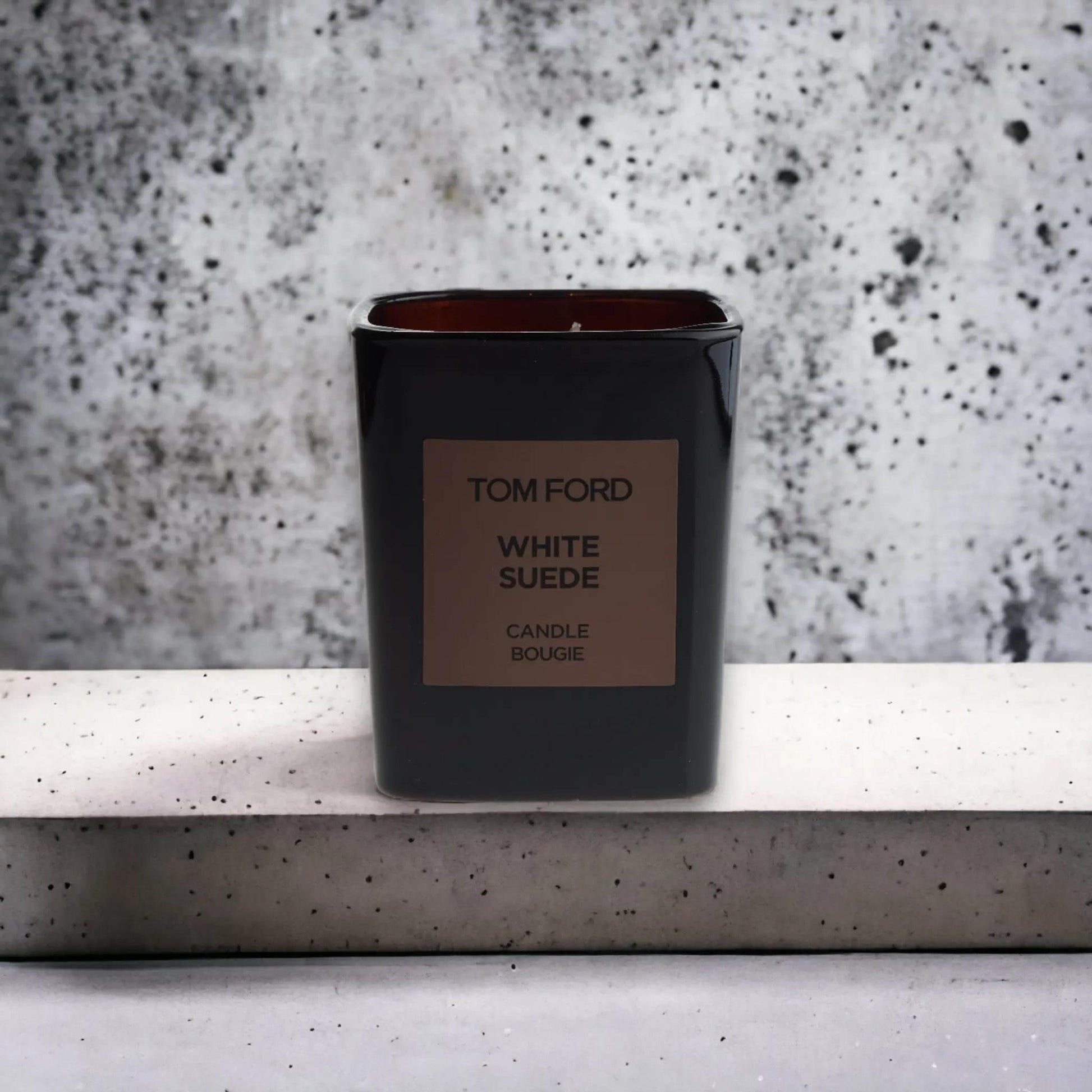 Luxuriöse Duftkerze in schwarzem Glas mit Label White Suede vor Betonhintergrund