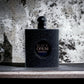 Schwarzer, glitzernder Parfumflakon Black Opium vor marmorierter Steinwand