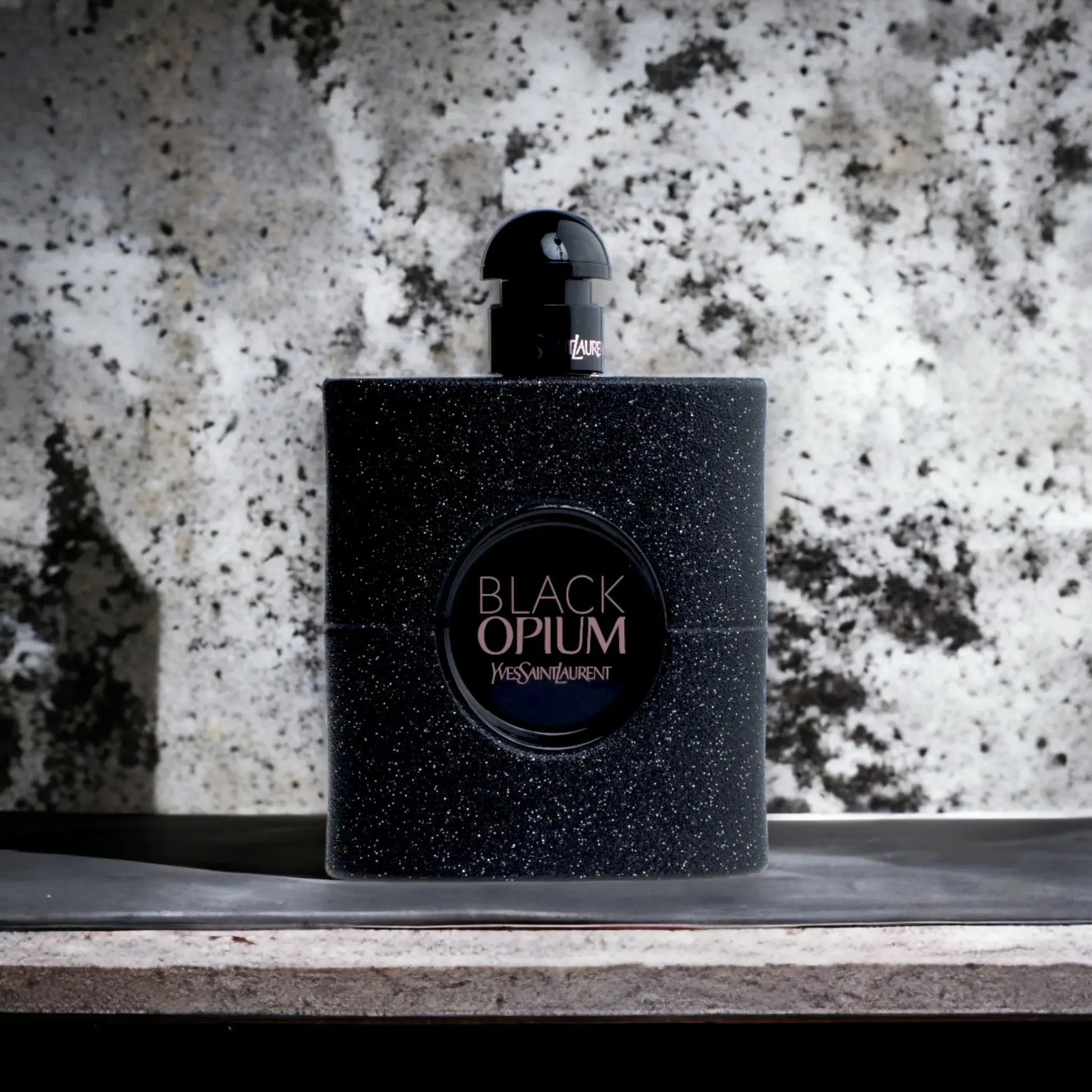 Schwarzer, glitzernder Parfumflakon Black Opium vor marmorierter Steinwand