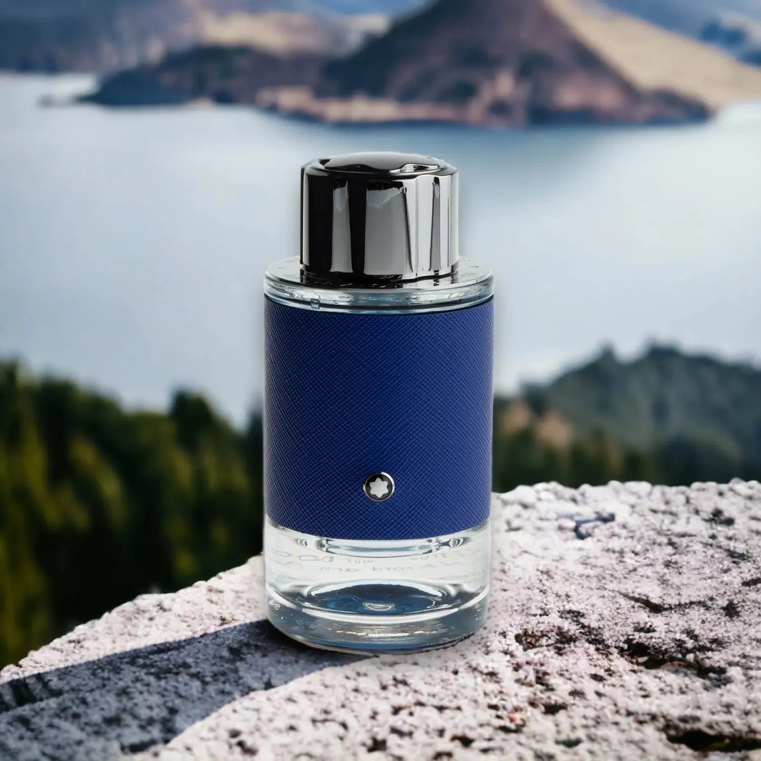 Blauer Parfumflakon steht auf einem Stein in Naturkulisse mit See und Bergen im Hintergrund.