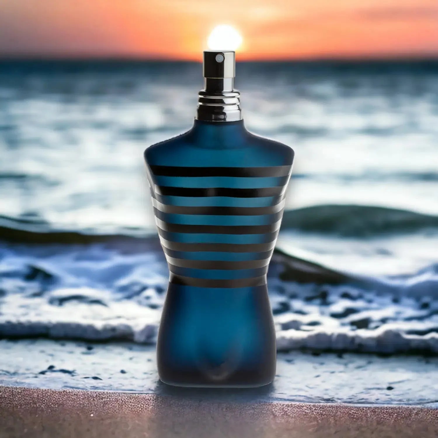 Blau-schwarzer Parfumflakon in Körperform am Strand vor Sonnenuntergang und Meer.