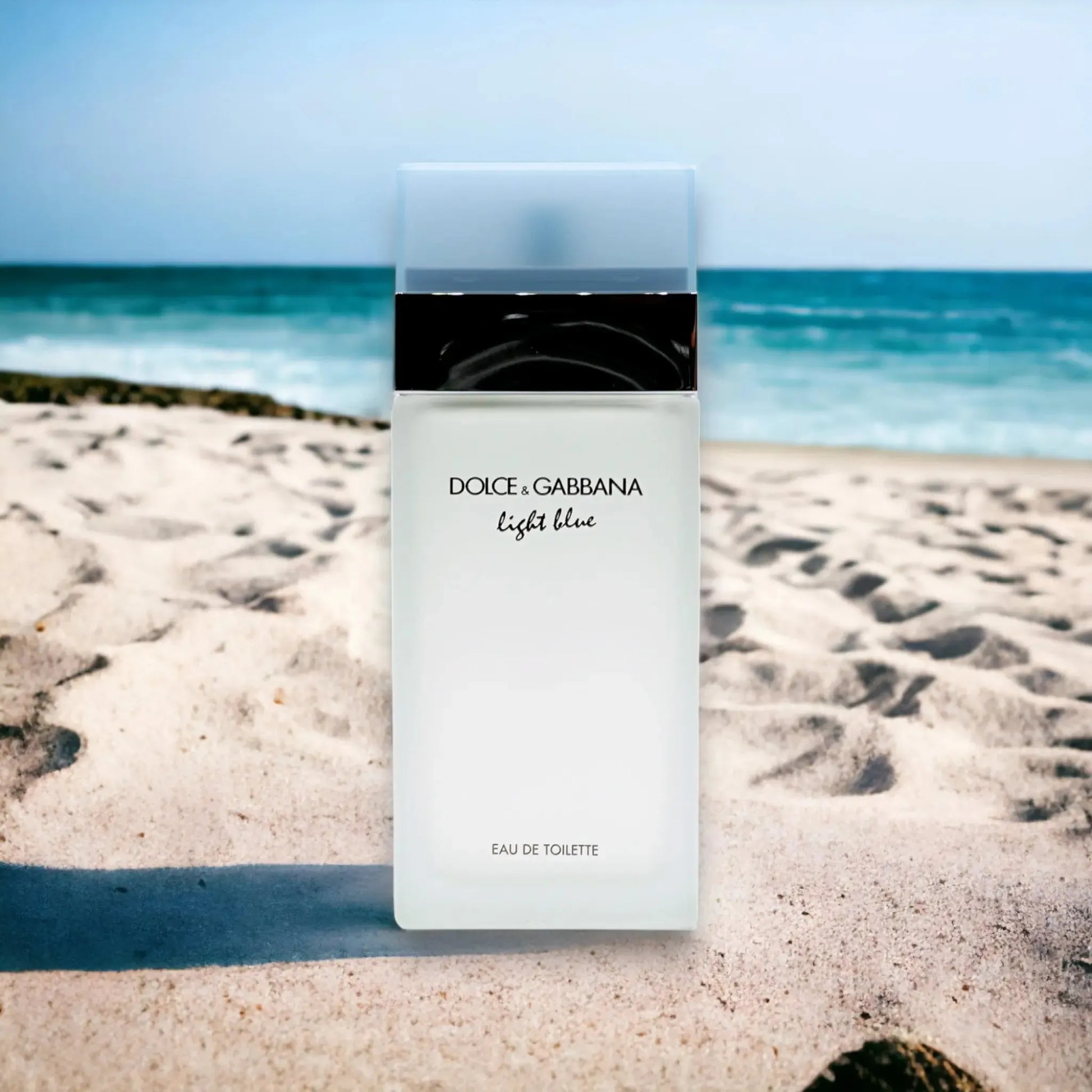 Parfümflakon Dolce & Gabbana Light Blue Eau de Toilette auf Sandstrand mit Meer im Hintergrund