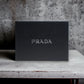 Schwarze Geschenkbox mit silbernem Prada-Logo, elegant auf Marmortisch platziert.