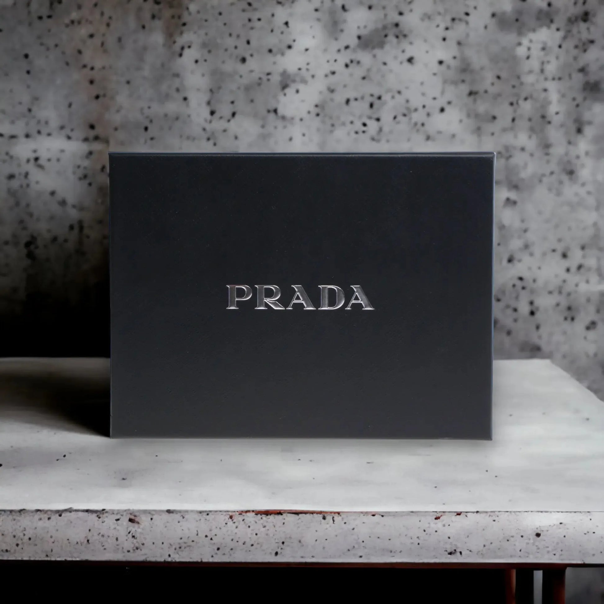 Schwarze Geschenkbox mit silbernem Prada-Logo, elegant auf Marmortisch platziert.