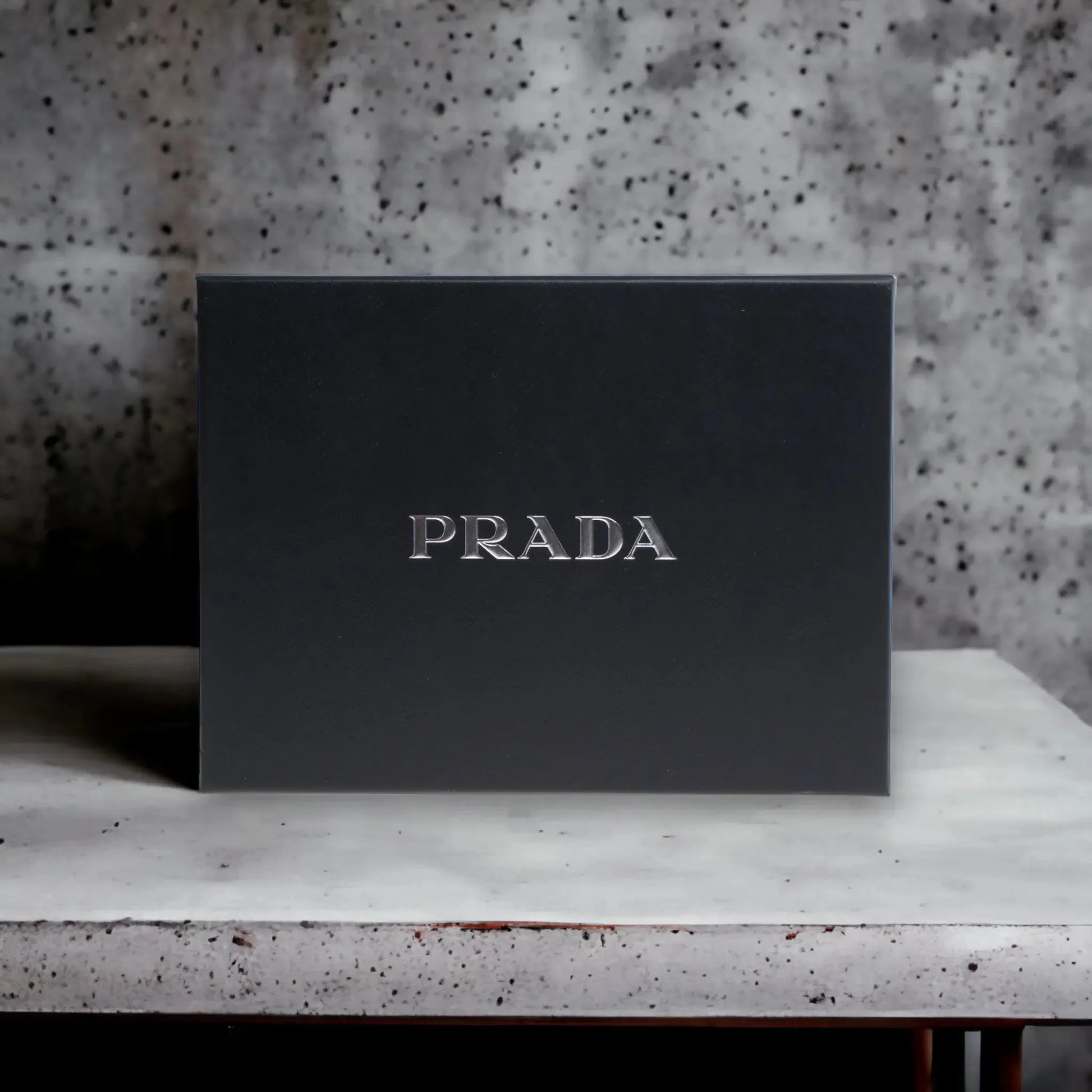Schwarze Prada Geschenkbox für Luxusparfum auf hellem Steintisch, minimalistisches Design