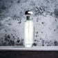 Transparenter Flakon Parfum mit silbernem Deckel vor marmorierter Steinwand