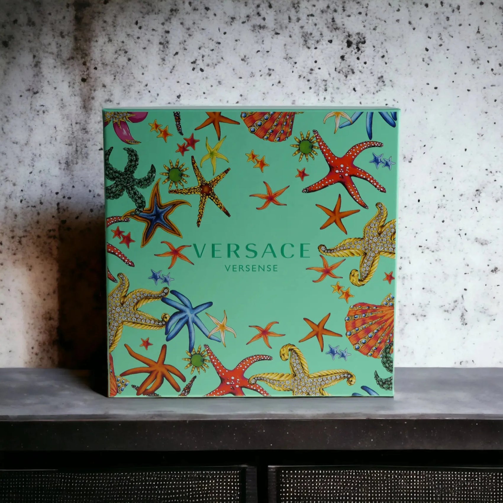 Versace Versense Duftset Verpackung, türkis mit bunten Seesternen, auf grauem Hintergrund